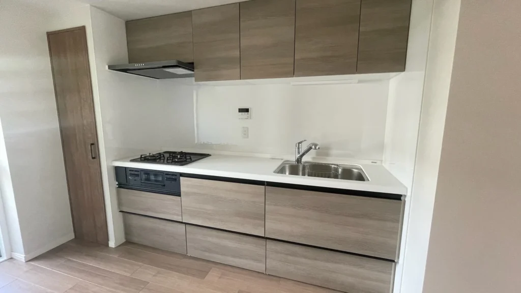 リノベーション後のキッチン。広いシンクと3口コンロが設置された、木目調の収納が特徴の清潔感ある空間。