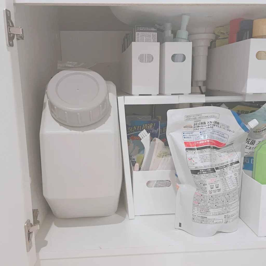 洗面台下の収納に置かれた白いポリタンクと洗剤詰め替えのストック