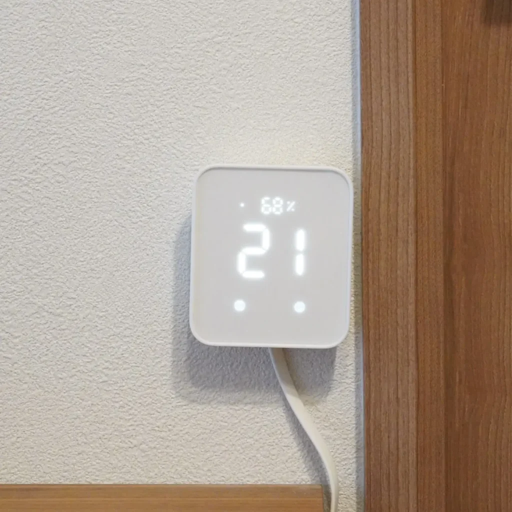 壁に設置したスイッチボットハブ2。室温21℃・湿度68％を表示中